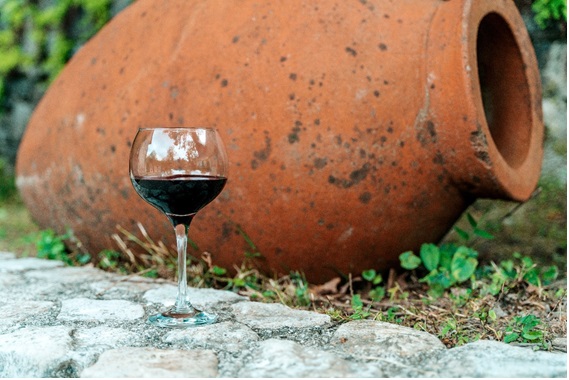 横たわるクヴェヴリの前に赤ワインのグラスが置かれている画像